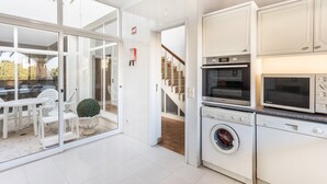 Een moderne keuken met inbouwapparatuur, een eethoek met witte meubels en een schuifdeur naar buiten.