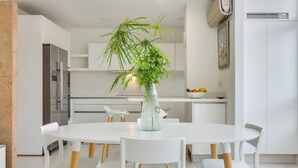 Una cocina moderna con armarios blancos, una mesa de comedor con sillas y una planta en maceta sobre la mesa.