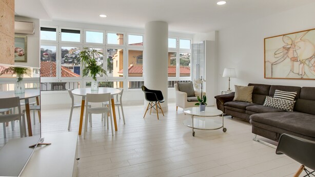 Amplia sala de estar con mesa de comedor, sillas, sofá y un amplio ventanal con vistas a edificios.