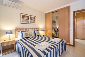 A hotel room with a bed, nightstands, a wardrobe, and a painting on the wall. - Holiday Apartment 'Apartment at Clube Praia da Oura' with Sea View (Albufeira)