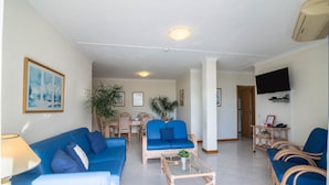 A living room with a blue sofa, a coffee table, wicker chairs, a television, and a framed picture on the wall. - Holiday Apartment 'Apartment at Clube Praia da Oura' with Sea View (Albufeira)