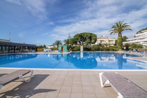En swimmingpool med liggestole, et overdækket område og en bygning med parabolantenne i baggrunden.