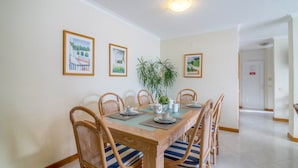A dining area with a wooden table, six chairs, a potted plant, and framed pictures on the wall. - Holiday Apartment 'Apartment at Clube Praia da Oura' with Sea View (Albufeira)