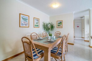 Un coin repas avec une table en bois, six chaises, une plante en pot et des tableaux encadrés au mur.