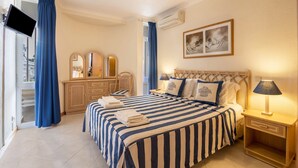 A hotel room with a bed, a TV, a desk, a chair, a wardrobe, and a painting on the wall. - Holiday Apartment 'Apartment at Clube Praia da Oura' with Sea View (Albufeira)