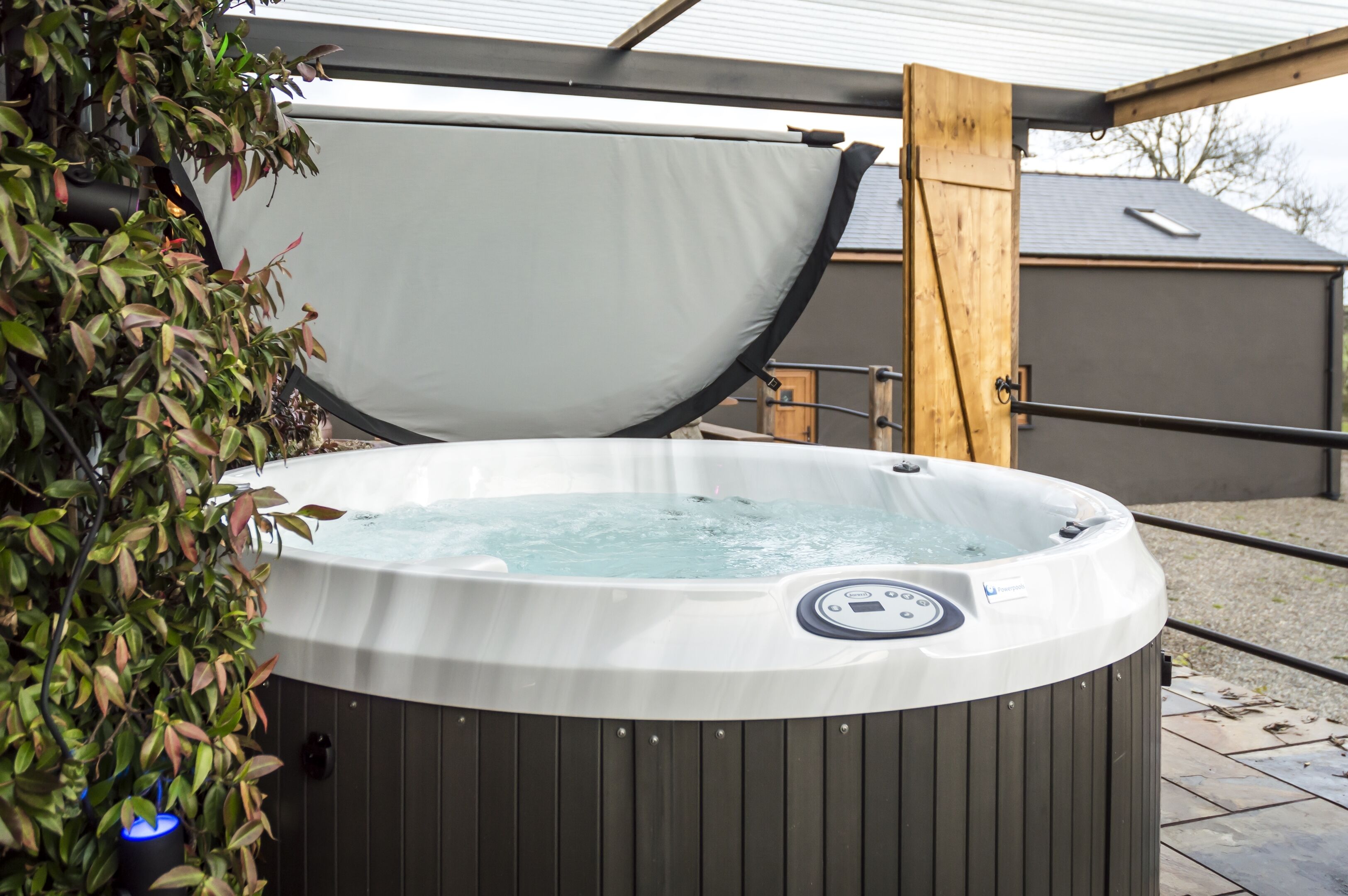 A hot tub with a wooden frame and a cover, surrounded by potted plants.