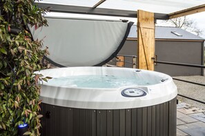 A hot tub with a wooden frame and a cover, surrounded by potted plants. - Lavender - Luxurious Barn Conversion (Haverfordwest)