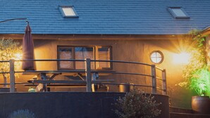 A building with a blue roof, a wooden fence, and a bench. There are potted plants and a table with chairs.