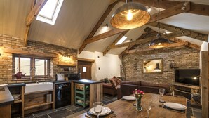A rustic kitchen with a wooden table set for dining, a stone fireplace, and a lofted ceiling with exposed beams.