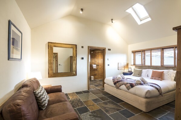 A spacious room with a large bed, a brown leather sofa, a mirror, and a skylight. - Lavender - Luxurious Barn Conversion (Haverfordwest)