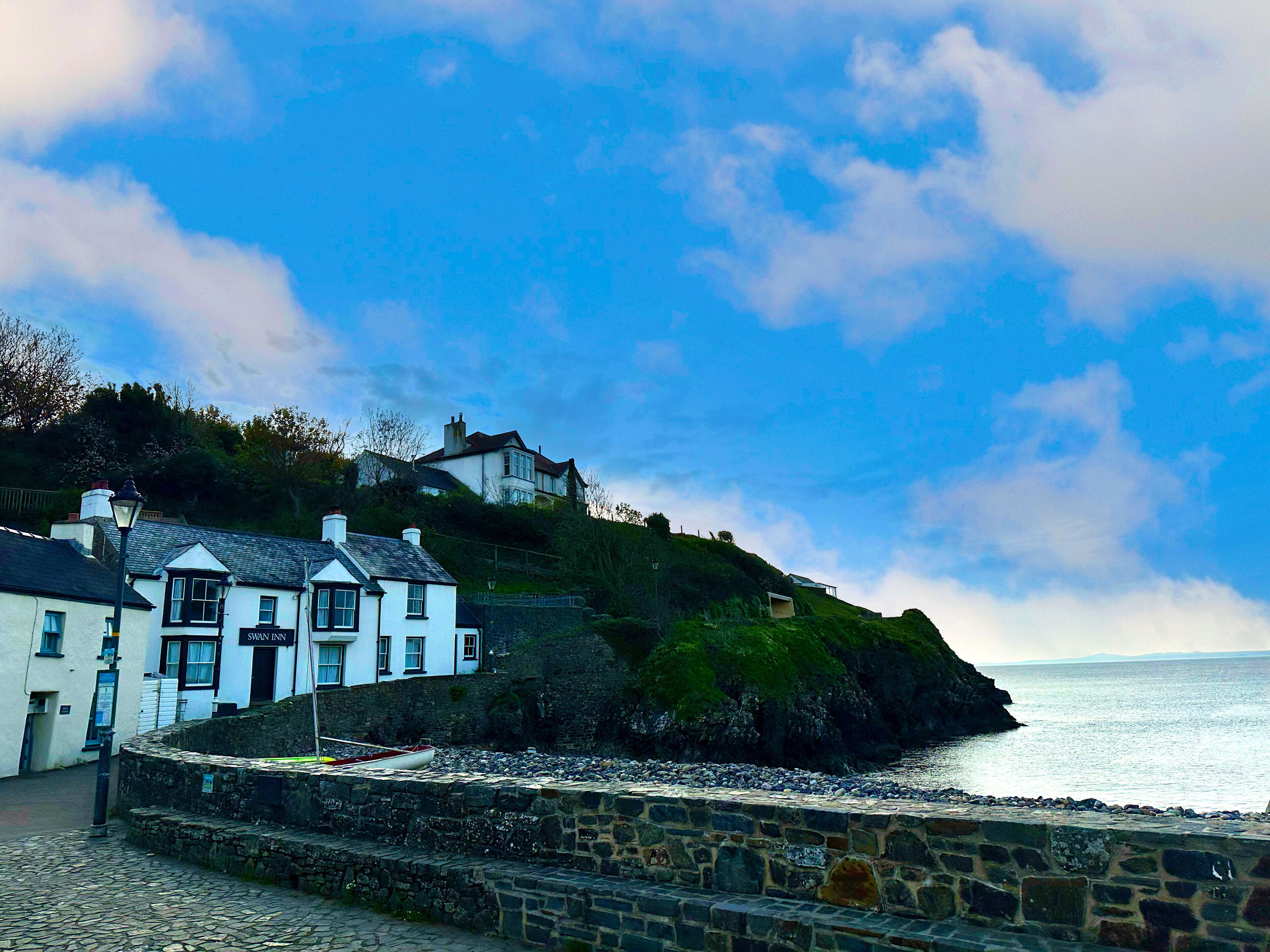 A coastal building with a stone wall and a boat docked in front.