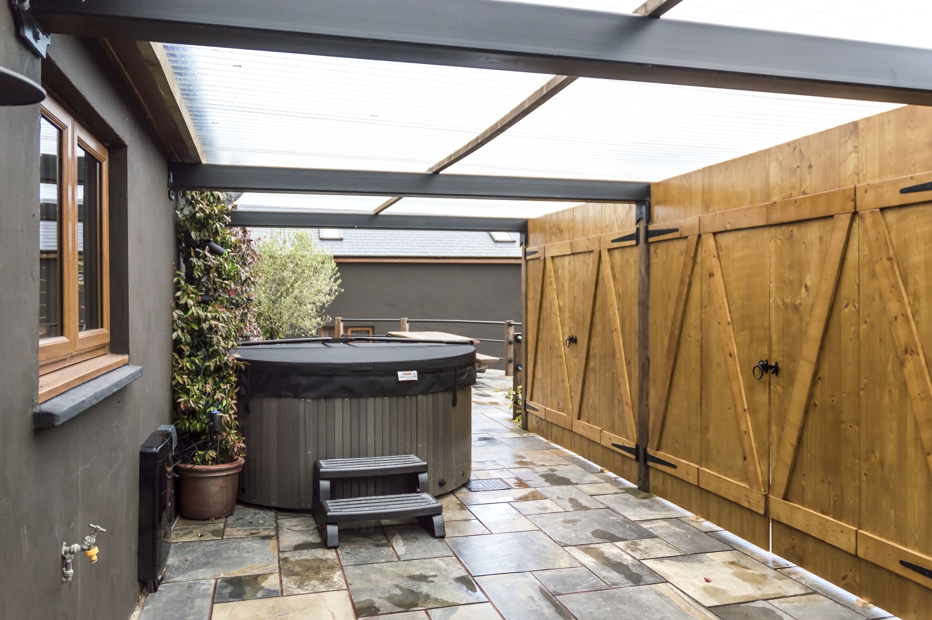 A patio with a hot tub, a wooden fence, and a stone floor.