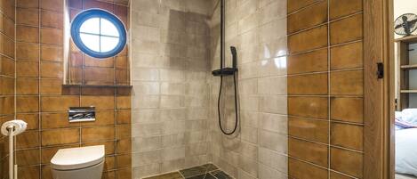 A bathroom with a shower, toilet, and a window.