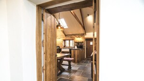 A rustic kitchen with stone flooring, wooden beams, and a hanging light fixture.