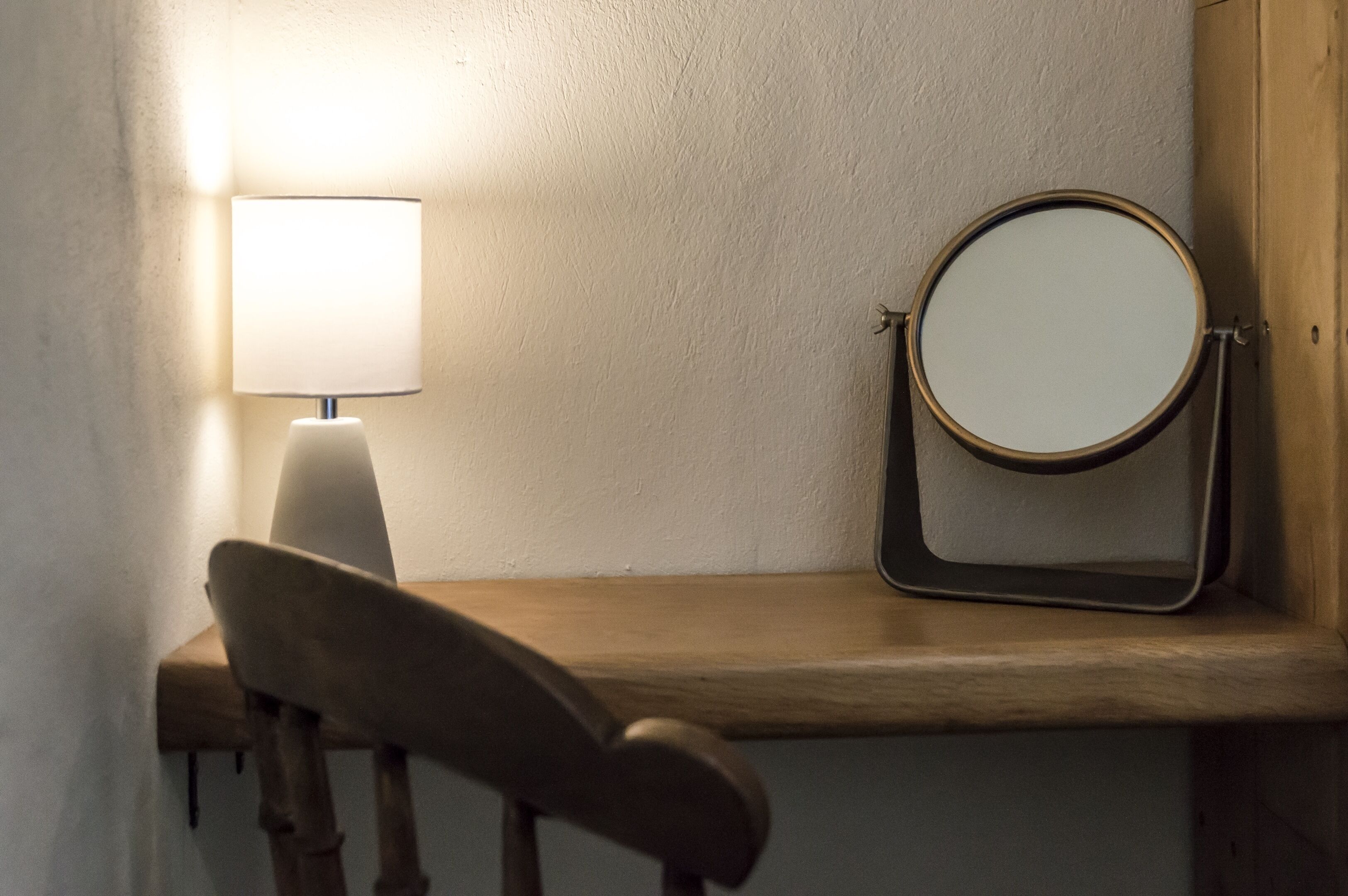 A wooden bench with a round mirror and a lamp against a textured wall.