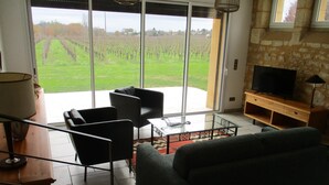 Una sala de estar con un sofá, dos sillones, una mesita de centro de vidrio y un televisor sobre un mueble de madera.