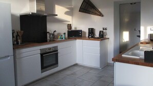 Una cocina moderna con armarios blancos, horno empotrado, microondas, cafetera y lámpara colgante.