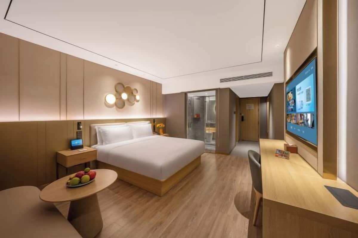 A modern hotel room with a bed, bedside table, and a desk with a computer.