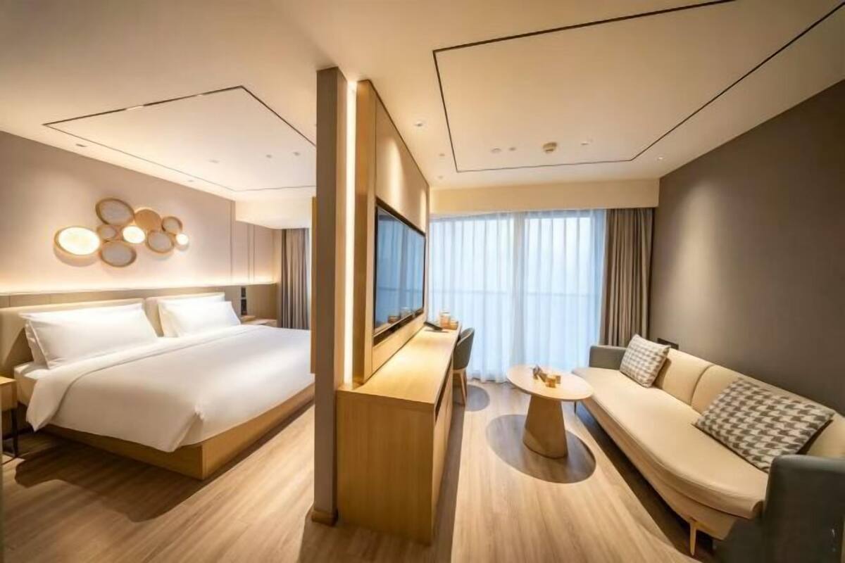 A modern hotel room with a large bed, a sofa, a small table, and a TV.