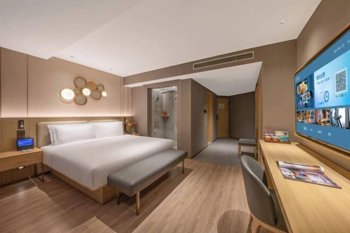 A modern hotel room with a large bed, bedside tables, a desk, and a TV displaying a QR code.