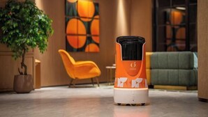A modern hotel lobby with a large potted plant, a vibrant orange chair, and a unique orange and white device on the floor. - Orange Hotel (Tianjin Wudadao) (Tianjin)