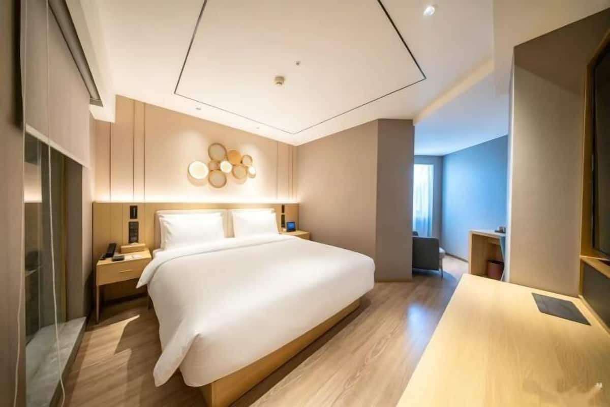 A modern hotel room with a large bed, bedside tables, a desk, and a wall-mounted light fixture.