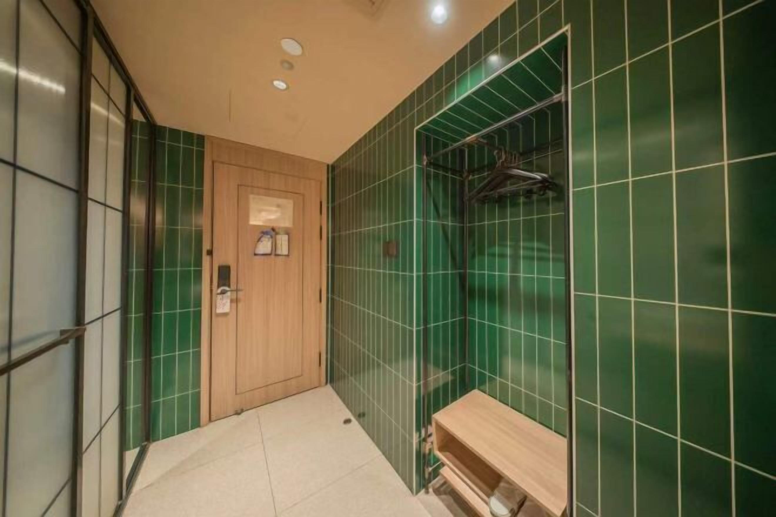 A narrow hallway with green-tiled walls, a wooden door, and a bench with a towel rack.