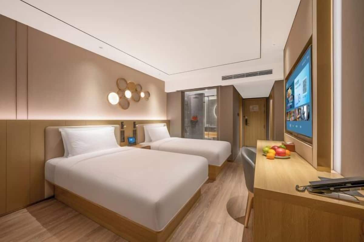 A hotel room with two beds, a desk, a TV, and a fruit bowl.