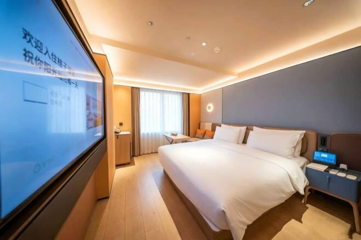 A hotel room with a large bed, bedside tables, a desk, and a TV screen.