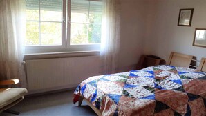 Un dormitorio con cama, una silla, un radiador y una ventana con persianas.