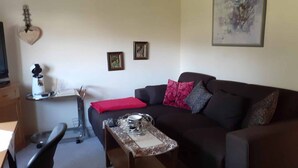 Una sala de estar con un sofá marrón oscuro, una mesita con una bandeja decorativa, un cojín rojo y dos cuadros en la pared.