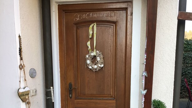 A wooden door with a wreath and a welcome sign. There are two potted plants on the steps and a metal grate in front of the door. - Ferienwohnung Heigemeir (Ehekirchen)