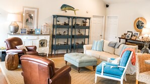A spacious living room with a high ceiling, a ceiling fan, and a large bookshelf filled with decorative items. - Coco’s Cabana (Deltaville)