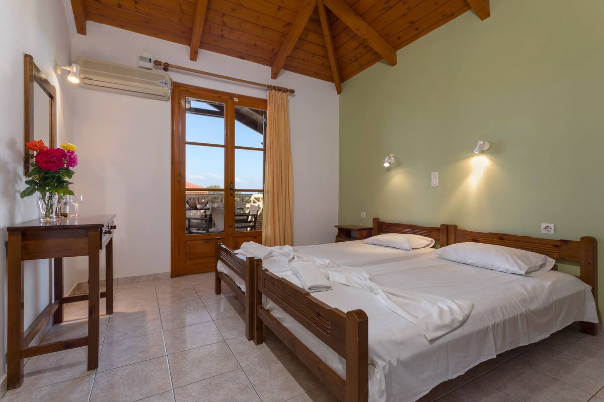 A bedroom with two beds, a wooden desk, a mirror, and a window with curtains.