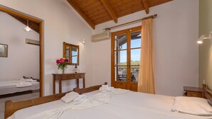 A hotel room with a large bed, a bathroom with a sink and mirror, and a view through a window with curtains. - Anemomylos Studios (Zakynthos)