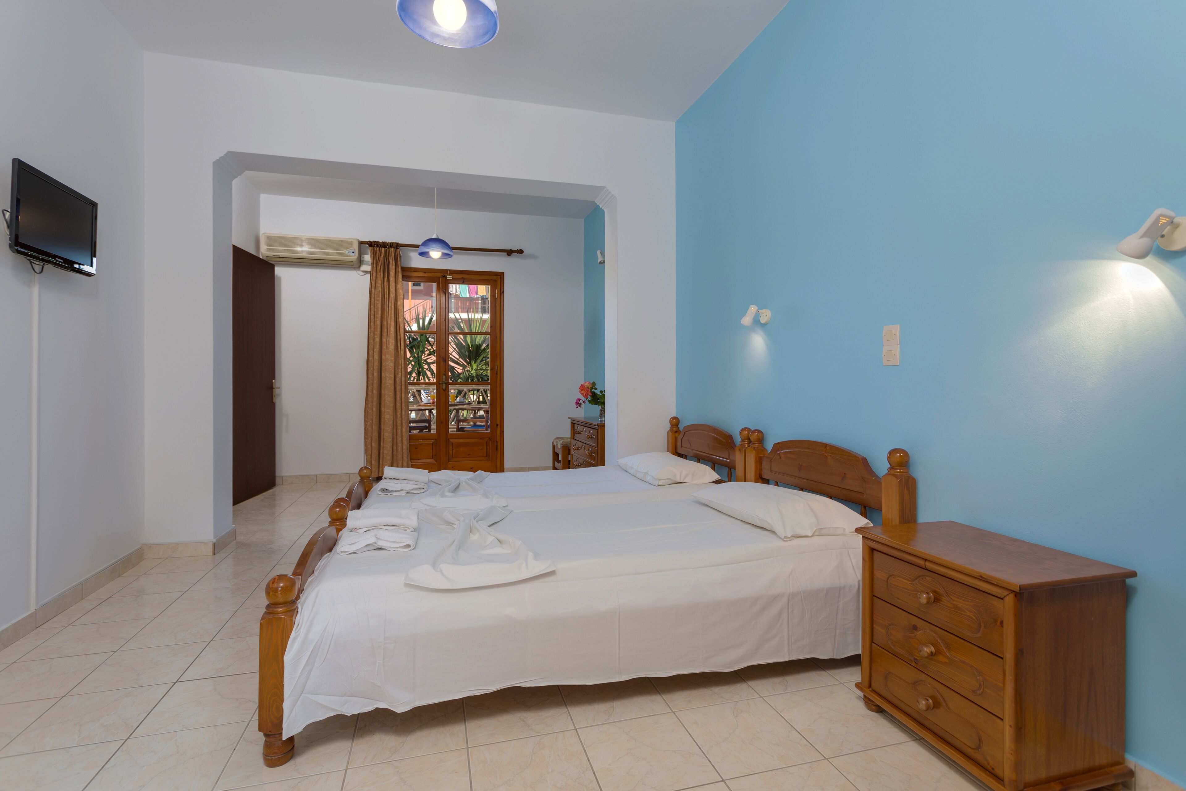 A bedroom with a large bed, wooden headboard, a dresser, and a television mounted on the wall.