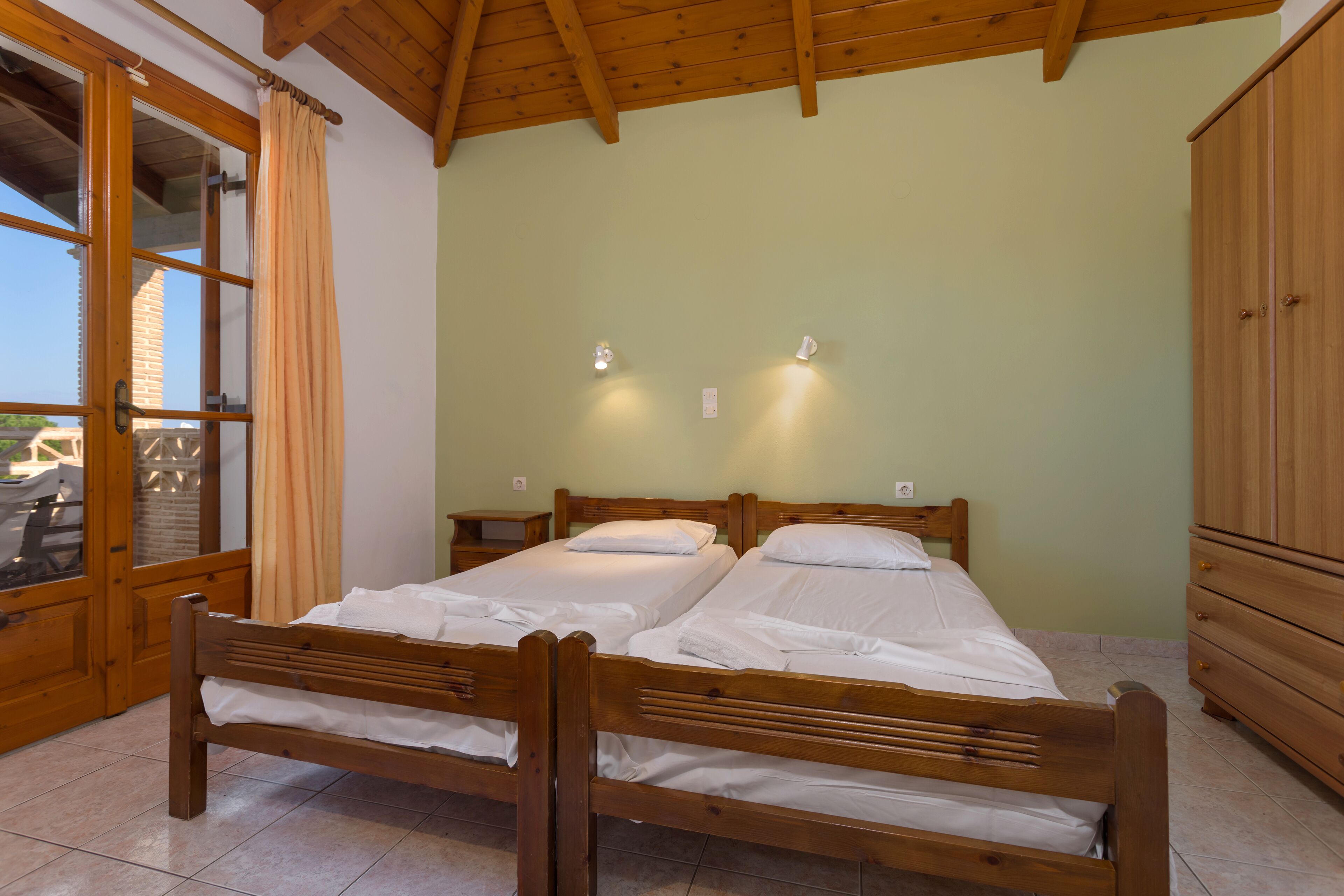 A room with two wooden beds, a wooden wardrobe, and a window with curtains.