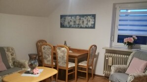 A living room with a wooden dining table, four chairs, a sofa, a small coffee table, and a patterned rug. - Ferienwohnung Anni (Dörfles-Esbach)