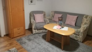 A room with a wooden wardrobe, a grey sofa with floral upholstery, and a small wooden table with a vase. - Ferienwohnung Anni (Dörfles-Esbach)