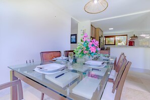 A dining area with a glass table set for four, surrounded by wooden chairs.