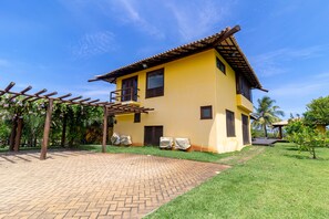 A yellow building with a tiled roof, a covered outdoor area with a pergola, and a paved walkway.