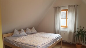 Makuuhuoneessa on yksi sänky, ikkuna, jossa on verhot, patteri ja ruukussa oleva kasvi.