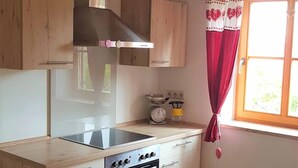 A kitchen with wooden cabinets, a stove, a sink, and a window with red curtains. - Ferienwohnung Abel (Heideck)