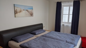 A bedroom with a bed, a headboard, a window with curtains, and a painting on the wall. - Ferienwohnung Abel (Heideck)
