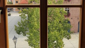 A window view of a building with a yellow facade, a stone tower, and a paved courtyard. - Ferienwohnung Abel (Heideck)