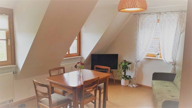 A cozy attic room with a dining table, chairs, a sofa, and a TV. - Ferienwohnung Abel (Heideck)