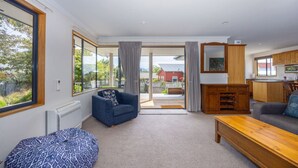 A spacious living room with a large window, a blue sofa, a wooden coffee table, and a view of the outside. - Mountain Views from Meadowstone (Wānaka)
