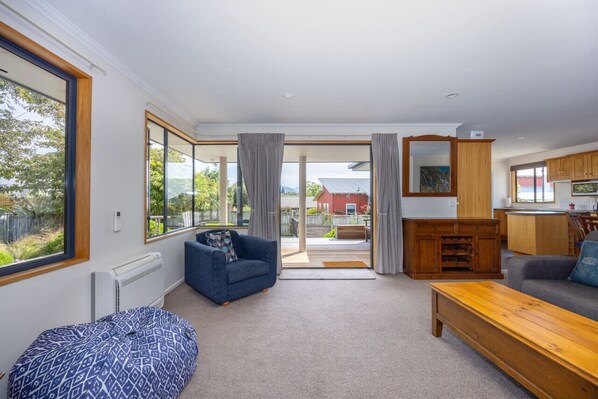 A spacious living room with a large window, a blue sofa, a wooden coffee table, and a view of the outside. - Mountain Views from Meadowstone (Wānaka)