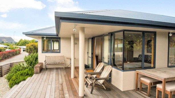 A modern house with a wooden deck, a covered patio area, and large glass windows. - Mountain Views from Meadowstone (Wānaka)