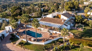 Une grande villa blanche dotée d’une piscine, entourée d’une végétation luxuriante et avec des montagnes en toile de fond.
